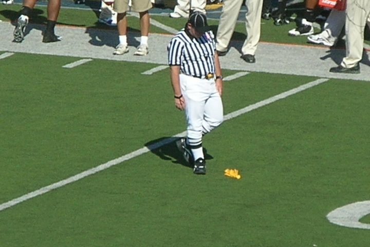 An official bending to pick up a flag after the whistle, players already walking away.
